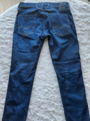 Mörkblå Replay jeans  - Snygga mörkblå jeans från Replay med raka ben och klassiska bakfickor med vit dekorativ söm. Jeansen har bälteshällor och är tillverkade i denim med en autentisk tvätt. Perfekta för en trendig och avslappnad look. W33 L32