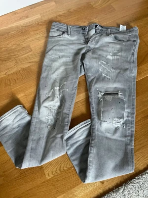 Grå slitna jeans - Säljer ett par grå jeans med slitningar och hål på benen. Jeansen har fem fickor, knappgylf och en cool, tvättad look. Perfekta för dig som gillar en avslappnad och trendig stil. 30/32 slim Glenn  hyfsat sällsynta 