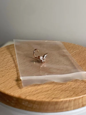 Roséguld 0.8mm piercing fjäril surgical steel - Oanvänd. Piercing i roséguldfärgat surgical steel med stenar i fjärilsform. 0.8mm, och 7mm lång. Får sanitation rengöring innan den skickas. 