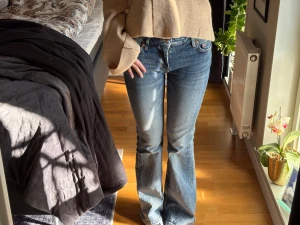 Blå bootcut jeans från weekday - Säljer ett par klassiska blå bootcut jeans från weekday med fem fickor och normal midja. Jeansen har en snygg tvättad look och subtila slitningar för en avslappnad vibe. Perfekta till sneakers eller boots och passar dig som gillar retrostil.