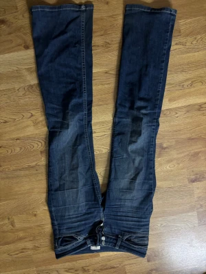 Mörkblå bootcut jeans med broderi - Snygga mörkblå bootcut jeans med ljusa slitningar och coolt broderi på bakfickorna. Klassisk femficksmodell med knapp- och dragkedjegylf. Perfekta för dig som gillar en avslappnad men trendig look.