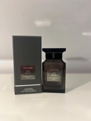 Tom Ford Oud Wood Eau de Parfum 100 ml - Tom Ford Oud Wood Eau de Parfum i en elegant mörkbrun glasflaska med svart lock. Flaskan rymmer 100 ml och har en stilren, lyxig design. Doften är känd för sina träiga och orientaliska noter, perfekt för dig som gillar exklusiva parfymer.