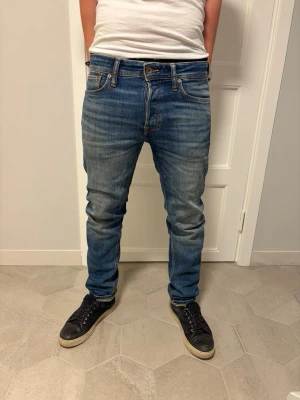 Jack & Jones jeans 👖  - Säljer ett par blå slim fit jeans med snygga slitningar och klassisk femficksdesign. Jeansen har en normal midja och är tillverkade i denim med stretch för extra komfort. Perfekt för dig som gillar en modern och avslappnad look.