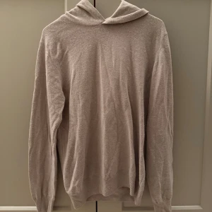 Oscar Jacobson Kashmir hoodie  - En stilren beige hoodie med huva och långa ärmar. Tillverkad i ett mjukt, stickat material som känns skönt mot huden. Perfekt för en avslappnad look och enkel att matcha med andra plagg. Ribbstickade muddar vid ärmslut och nederkant.