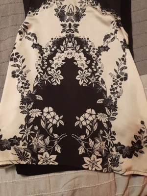 Svartvit blommig topp  - Snygg svartvit top med ett detaljerat blommönster. Klänningen har en rak passform och är tillverkad i ett mjukt, lätt material som känns skönt mot huden. Perfekt för dig som gillar stilrena kontraster och unika mönster.