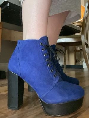 Blåa platåstövletter med snörning - Snygga stövletter i klarblå mocka-look med kraftig platå och hög blockklack. Skorna har snörning framtill med svarta skosnören och metallöljetter. Perfekta för dig som vill sticka ut med färg och höjd. Materialet ser ut som mocka och klacken är svart.