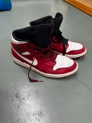 Air Jordan 1 Mid Chicago - Säljer ett par Air Jordan 1 Mid Chicago i röd och vit färg med svarta detaljer. Ovandelen är i läder och har röda och svarta skosnören. Perfekta för dig som gillar streetwear. Knappt använda.
