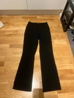 Svarta kostymbyxor från BikBok - Snygga svarta kostymbyxor från BikBok med klassisk rak passform och lätt utsvängda ben. Byxorna har hällor för skärp och är perfekta för en stilren look. Materialet känns mjukt och följsamt.