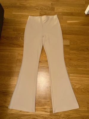 Beiga utsvängda mjukisbyxor H&M - Snygga beiga mjukisbyxor från H&M med utsvängda ben och hög midja. Byxorna är i ett mjukt och stretchigt material som känns skönt mot huden. Perfekta för en chill och trendig look.