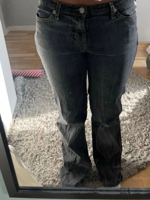 Mörkgrå bootcut jeans med slitningar - Säljer ett par mörkgrå bootcut jeans med klassiska femficksdetaljer och slitningar längs benen. Jeansen har en låg midja och är tillverkade i denim med stretch för skön passform. Perfekta för dig som gillar en avslappnad och trendig look.