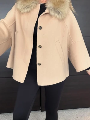 Zara hand made kort jacka - Kort beige kappa med bred krage i fuskpäls med 4 stora knappar framtill. Pälskragen kan man ta bort. Modellen är vid med trekvartsärmar och har två snedställda fickor. Perfekt till våren just nu:)