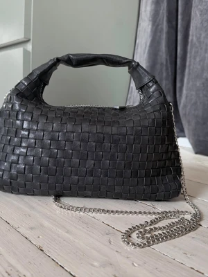Núnoo Dandy väska i svart läder - Snygg flätad väska från Núnoo i modell dandy, bär den i handen eller med kedjan på axeln / crossbody. ~ 30cm bred. Så gott som oanvänd. Djur- och rökfritt hem. Nypris 182