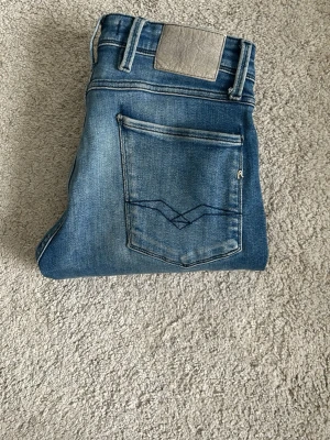 Blå jeans från Replay - Snygga blå jeans från Replay med klassisk femficksdesign och coolt broderi på bakfickan. Jeansen har en ljus tvätt och är tillverkade i bomull med lite stretch för skön passform. Perfekt för dig som gillar en avslappnad och trendig look.