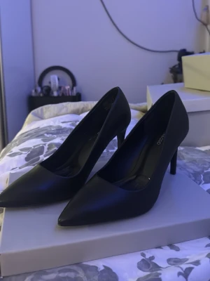 Svarta pumps  - Stilrena svarta pumps, storlek 39. Skorna har spetsig tå, smal klack och är gjorda i ett slätt material som ger en elegant vibe. Perfekta för dig som gillar klassiska och tidlösa skor