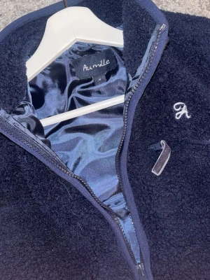 Mörkblå ullväst från Aumille - Mysig mörkblå ullväst från Aumille med glansigt innerfoder och dragkedja framtill. Västen har två fickor med dragkedja och en liten broderad logga på bröstet. Perfekt för lager på lager och riktigt skön att bära. Strl:S och är helt oanvänd, inget tecken på användning och luktar helt ny, köpt för 1299 från företaget aumille men säljs för endast 879kr.