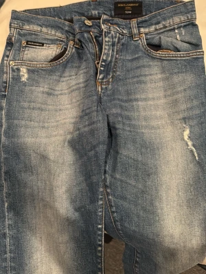 Dolce & Gabbana ljusblå slim jeans - Säljer ett par ljusblå slim fit jeans från Dolce & Gabbana med slitna detaljer och snygg tvätt. Klassisk femficksmodell med dragkedja och knapp. Jeansen har en modern passform och coola slitningar för en trendig look.