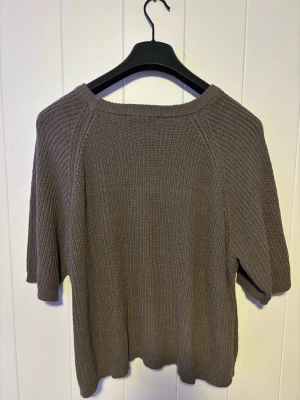 Brun stickad tröja med kort ärm - Säljer en enkel och stilren brun stickad tröja med korta ärmar och rund hals. Tröjan har en rak passform och är gjord i ett mjukt, grovt stickat material. Perfekt att matcha med jeans eller kjolol för en avslappnad look. 