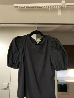 Svart topp med puffärmar - Svart topp med puffiga korta ärmar och rund halsringning. Tillverkad i mjuk bomull som känns skön mot huden. 