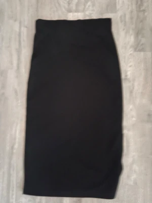 Svart långkjol med slits - En stilren svart långkjol med slits på sidan. Kjolen har en rak och enkel design som gör den lätt att matcha med olika toppar. Perfekt för dig som gillar minimalistisk stil och vill ha en kjol som funkar till många tillfällen.