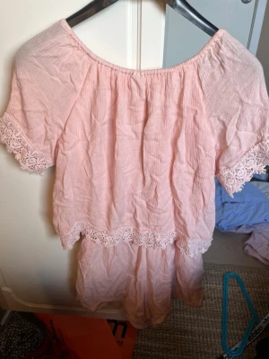 Ljusrosa byxdress från Lindex Kids - Söt ljusrosa byxdress från Lindex Kids med korta ärmar och spetsdetaljer vid ärmslut och midja. Byxdress har en luftig och avslappnad passform, perfekt för varma dagar. Tillverkad i mjukt bomullstyg.