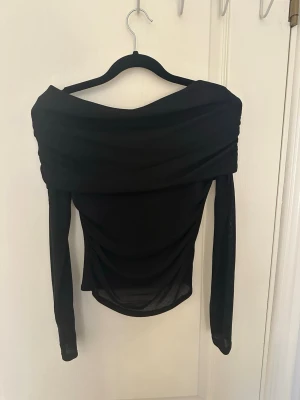 Svart offshoulder tight topp - Trendig svart figursydd offshoulder topp med långa ärmar. Snygg draperad design över axlarna och figurnära passform. Endast använd 1 gång, därav i fint skick. Skulle säga att den även passar för storlek S. Man kan även justera hur mycket/lite offshoulder men vill ha. Hör av er vid funderingar!💗