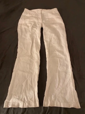 linnebyxor - Säljer ett par vit linnebyxor med vida ben och låg midja. Byxorna har två framfickor och stängs med dragkedja och knapp. Perfekta för en avslappnad och stilren look. Materialet är svalt och 100% linne.