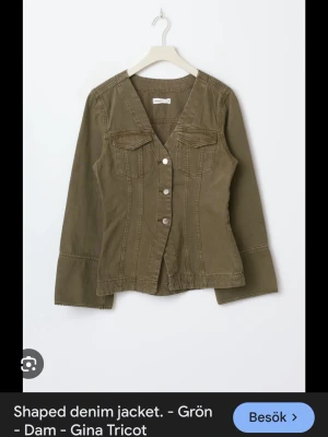 Grön jeansjacka från Gina Tricot - Snygg grön jeansjacka från Gina Tricot med figurnära passform, V-ringning och dekorativa sömmar. Jackan har två bröstfickor med lock och silverfärgade knappar framtill. Perfekt för dig som vill ha en unik twist på den klassiska jeansjackan.