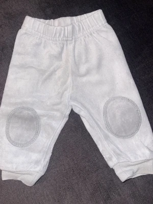 Grå mjukisbyxor från H&M baby - Supermjuka grå mjukisbyxor från H&M med resår i midjan och förstärkta knän. Perfekta för chill dagar eller lek. Tillverkade i bomullsmix för extra komfort och stretch. Snygg och enkel design med ribbade muddar vid benslut.