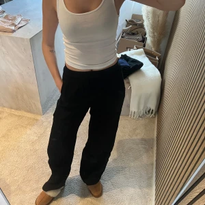 Vit ribbad linnetopp i bomull - Säljer en vit ribbad linnetopp i bomull med smala axelband och tight passform. Perfekt att styla med jeans eller kjol för en enkel och fräsch look. Toppen är ärmlös och har en klassisk, rund halsringning.