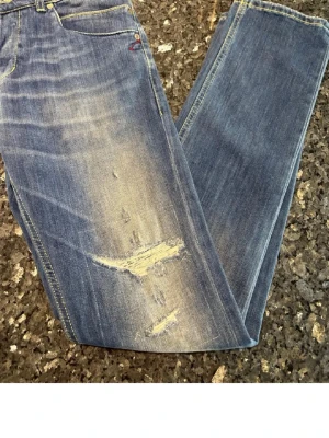 Blå slitna jeans med ljusa detaljer - Säljer ett par blå jeans med slitningar och ljusa partier framtill. Jeansen har klassisk femficksmodell och raka ben. Perfekta för en avslappnad och trendig look.