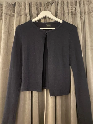 Mörkblå kofta från Gina Tricot - Stilren mörkblå kofta från Gina Tricot med rund halsringning och lång ärm. Modellen är kortare i passformen och har en enkel, öppen framsida utan knappar. Perfekt att slänga över en topp för en clean look.