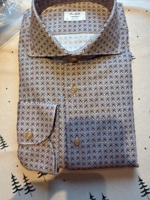 Mönstrad skjorta från Van Gils - Snygg skjorta från Van Gils med smått geometriskt mönster i blått och brunt på beige botten. Klassisk krage, knäppning framtill och långa ärmar. Perfekt för dig som vill sticka ut lite extra med stilren design.