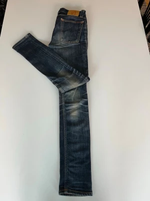 Blå Nudie Jeans Slim - Säljer ett par blå slim fit jeans från Nudie Jeans med snygga slitningar och tvättade detaljer. Modell - High Kai - W28 L32