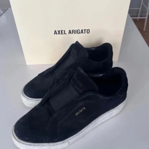 Svarta sneakers från Axel Arigato - Stilrena svarta sneakers från Axel Arigato i mocka med vit sula och diskret logga på sidan. Skorna har en minimalistisk design utan snörning och en låg silhuett som passar till många olika outfits. Kommer med originalpåse och box. Hör av dig vid minsta intresse!✨⭐️