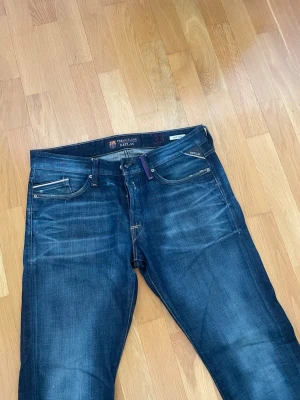 Mörkblå Replay jeans herr - Säljer ett par snygga mörkblå jeans från Replay med klassisk femficksmodell och diskreta slitningar framtill. Jeansen har raka ben och detaljer i silverfärg på fickorna. Materialet är mjukt denim med en skön passform. Perfekta för en avslappnad stil.