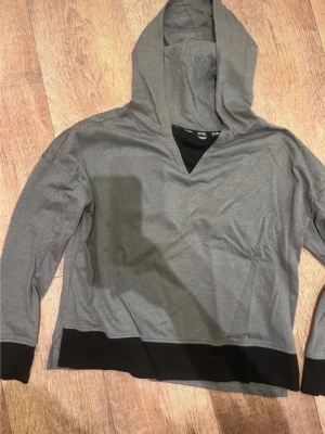 Grå hoodie med svarta detaljer - Snygg grå hoodie från H&M med svarta muddar och svart detalj vid halsen. Tröjan har en klassisk huva och är tillverkad i mjukt bomullsmaterial. Perfekt för en avslappnad och trendig stil.