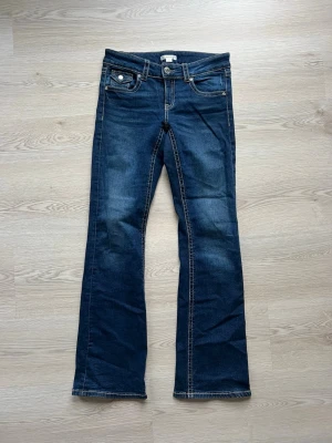 Mörkblå bootcut jeans med fickdetalj - Snygga mörkblå bootcut jeans med kontrastsömmar och unik fickdetalj framtill. Jeansen har klassisk femficksdesign och är tillverkade i ett slitstarkt denimtyg. Perfekta för dig som gillar en retroinspirerad look. I storlek 164 på gina young men passar mig som brukar ha 36 i jeans! 