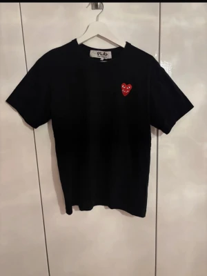 Svart Comme des Garçons PLAY t-shirt - Svart t-shirt från Comme des Garçons PLAY med det ikoniska röda hjärtat broderat på bröstet. Klassisk rund hals och korta ärmar. Tillverkad i mjuk bomull för en skön känsla och enkel stil.