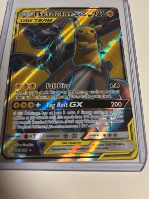 Pokémonkort Pikachu & Zekrom GX - Unikt Pokémonkort med Pikachu & Zekrom GX TAG TEAM. Kortet har holografisk yta med guld, svart och blått motiv. Text och attacker på engelska, 240 HP. Kortet är i plastfodral och är perfekt för samlare eller Pokémonentusiaster. Rare 162/181. Pokemon 2019!