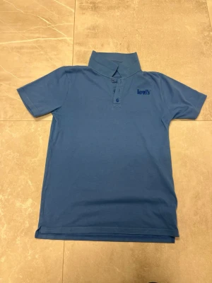 Blå kortärmad skjorta från Levi's - Snygg blå skjorta från Levi's med korta ärmar och klassisk krage. Skjortan har knappar framtill och en diskret Levi's-logga på bröstet. Tillverkad i mjuk bomull som känns skön mot huden. Perfekt för en avslappnad och stilren look.