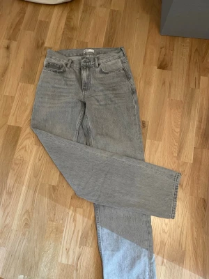 Grå raka jeans från Weekday - Säljer ett par grå jeans från Weekday med klassisk femficksdesign och raka ben. Jeansen har hög midja och är tillverkade i ett slitstarkt denim-material. Perfekt för dig som gillar en enkel och stilren look.