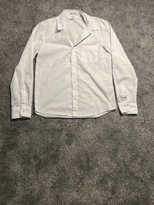 Vit klassisk skjorta från Hm - Säljer en vit skjorta från Hm med klassisk krage och bröstficka. Skjortan har långärmad design och knappar framtill. Perfekt för dig som gillar en clean och enkel stil.