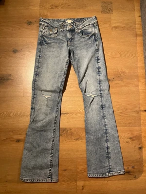 Ljusblå bootcut jeans med slitningar Gina Tricot - Säljer ett par ljusblå bootcut jeans från Gina Tricot med snygga slitningar på båda benen. Jeansen har klassisk femficksdesign och är tillverkade i denim. Perfekta för en avslappnad och trendig look. 