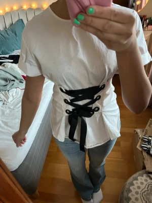 Vit topp med svart snörning - Säljer en snygg vit topp med bred svart snörning framtill. 