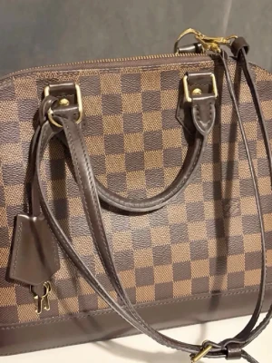 Äkta Louis Vuitton PM Damier handväska  - Säljer en klassisk Louis Vuitton handväska i Damier Ebene-mönster. Väskan är brun med mörkbruna läderdetaljer, guldfärgade metalldelar och har både handtag och axelrem. Allt är inkluderat förutom självaste boxen och självklart medföljs äktighetsbevis med kvitto. Mycket litet slitage på axelbandet, men i helhet är i väskan som ny och välbehållen. 
