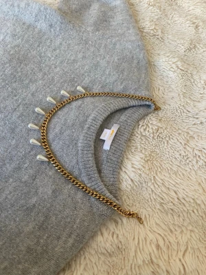 Guldfärgat halsband med pärldroppar - Snyggt halsband i guldfärgad rostfritt med droppformade vita pärlor som hänger längs kedjan. Perfekt statement-piece för att lyfta vilken outfit som helst. Kedjan har en chunky känsla och pärlorna ger en elegant touch.