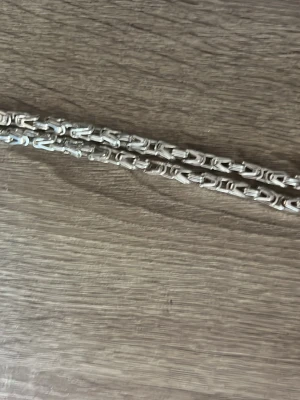 Silverfärgat kedjehalsband - Säljer ett stilrent halsband i silverfärg med unika, rektangulära länkar som ger ett coolt och modernt intryck. Halsbandet är tillverkat i metall och passar perfekt för dig som gillar att sticka ut med accessoarer.