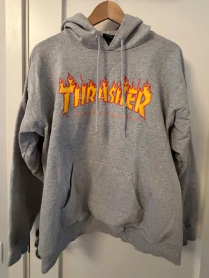 Grå Thrasher hoodie - Säljer en grå hoodie från Thrasher. Perfekt för dig som gillar streetwear och skatekultur. Defekter framkommer på bilderna. Köpt på junkyard.