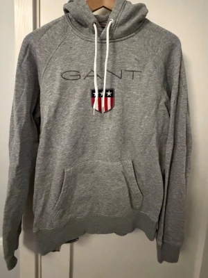 Grå hoodie GANT - Grå hoodie från GANT med stort tryck på framsidan.