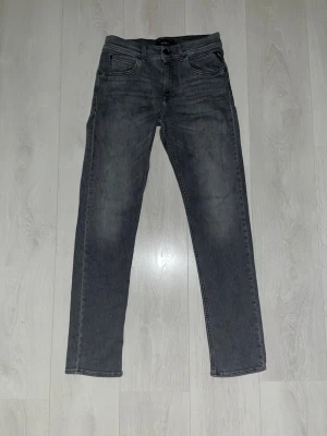 Grå raka jeans från Replay - Säljer ett par grå jeans från Replay med rak passform och klassisk femficksdesign. Jeansen har svarta sömmar och en snygg tvättad look. Materialet är denim och de har bälteshällor samt knappgylf. Perfekta för en avslappnad stil.                   Nytt pris: 899